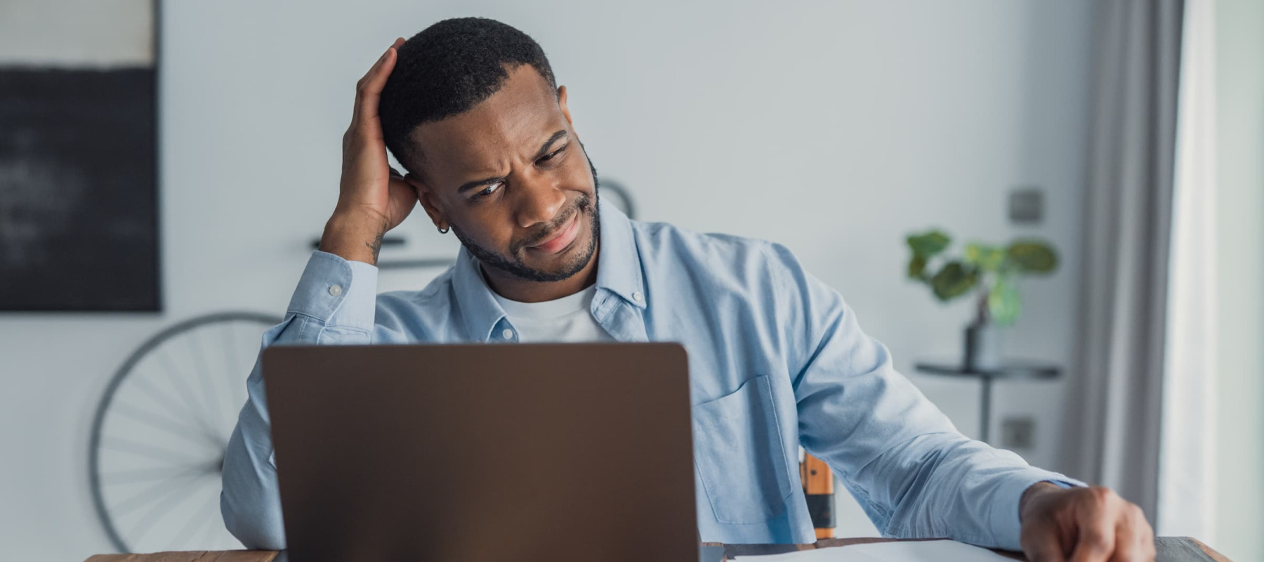 A photo of a man confused looking at his laptop