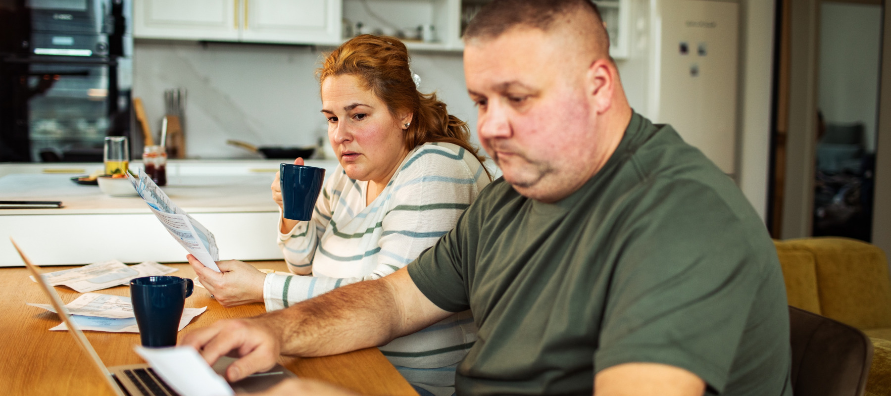 A concerned couple reviewing bills at home at their kitchen table.