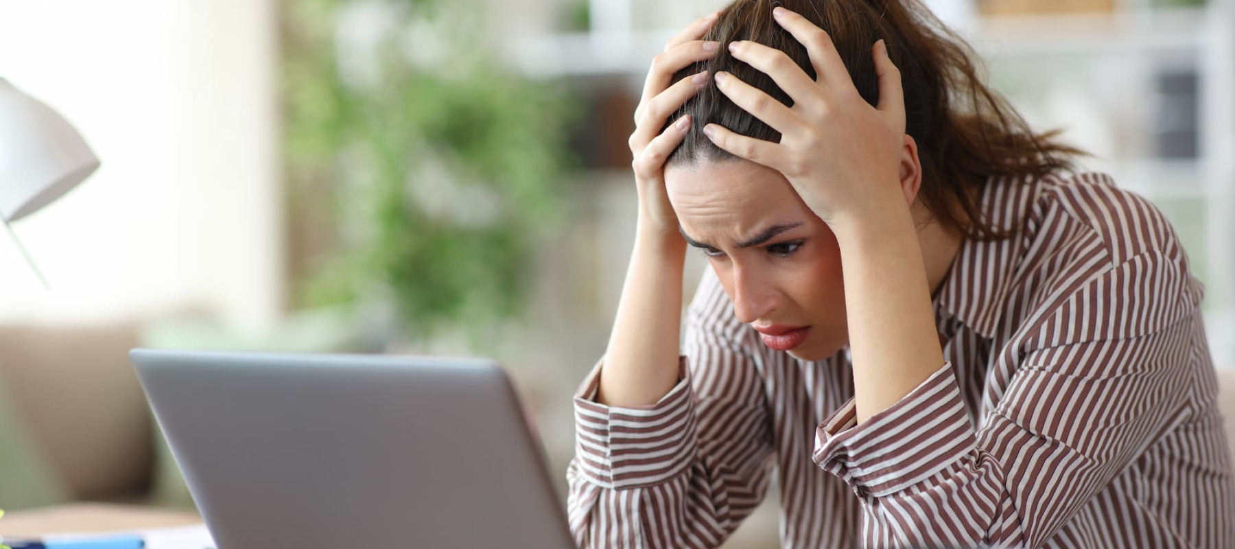 A photo of a woman stressed, looking at a laptop