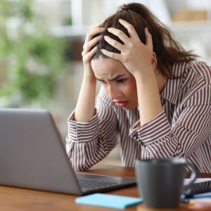 A photo of a woman stressed, looking at a laptop