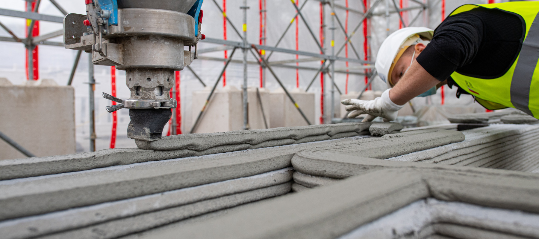 A construction worker observes as a 3D printer creates a wall using concrete.