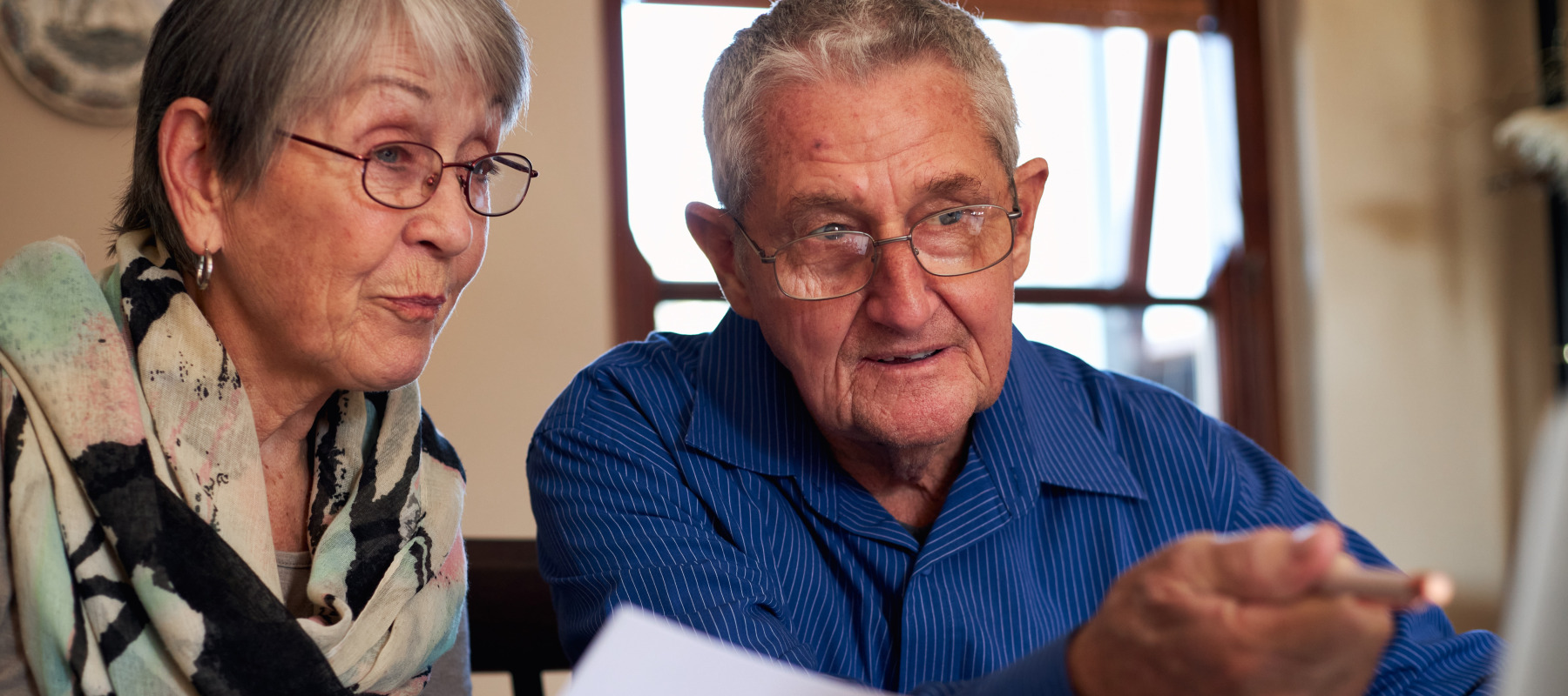 Older couple at home checking personal finances on laptop.