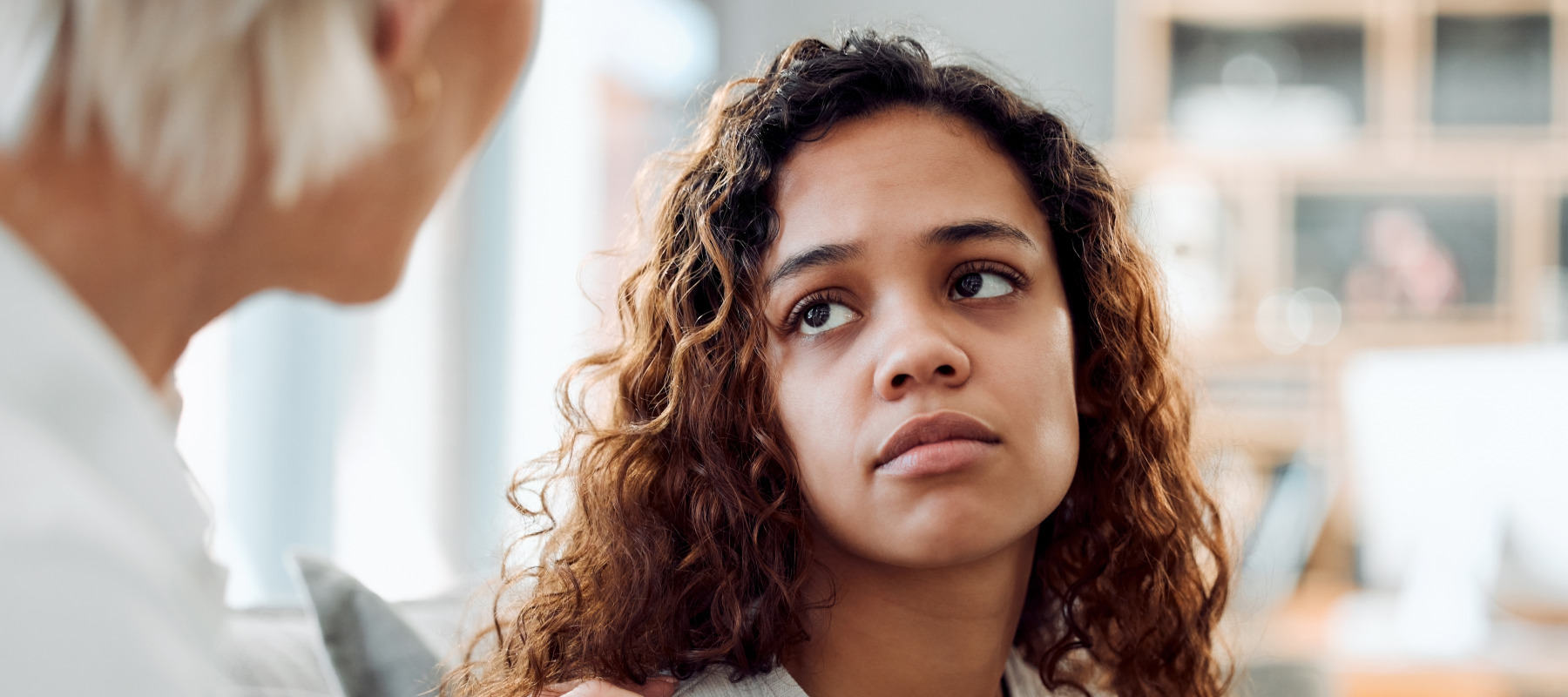 Young woman looks at someone with their hand on her shoulder, looking distressed and unhappy.