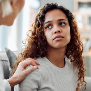 Young woman looks at someone with their hand on her shoulder, looking distressed and unhappy.