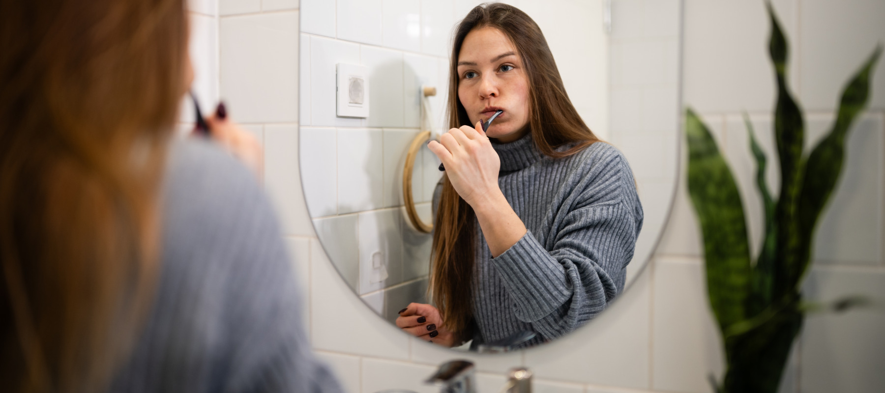 A woman brushing her teeth in front of the mirror.