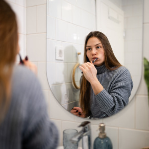 A woman brushing her teeth in front of the mirror.