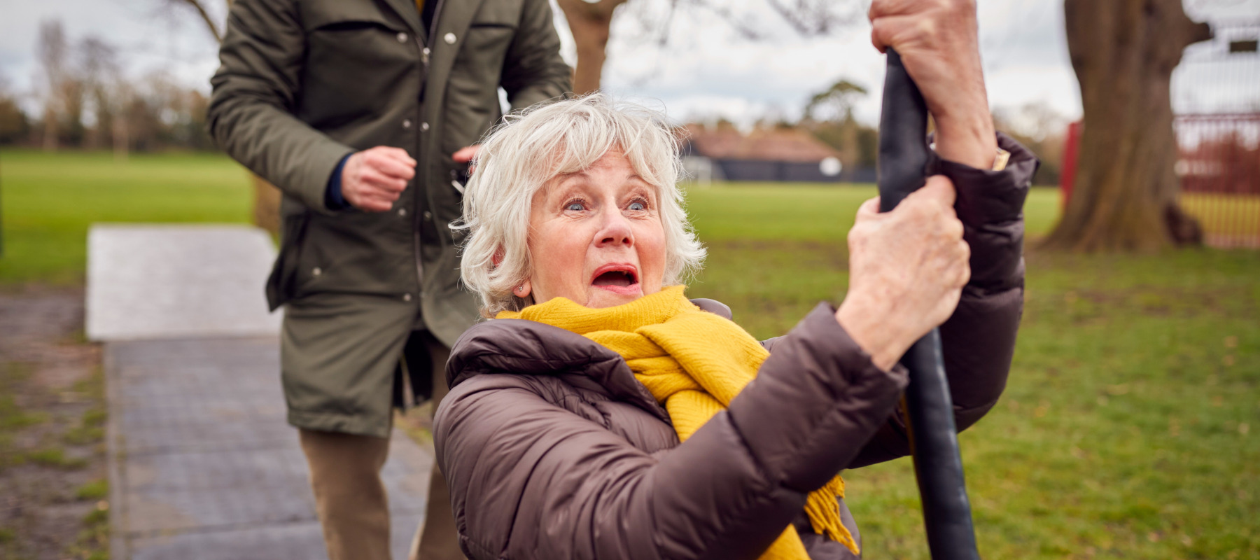 Senior woman playfully rides on a zipline at the park.