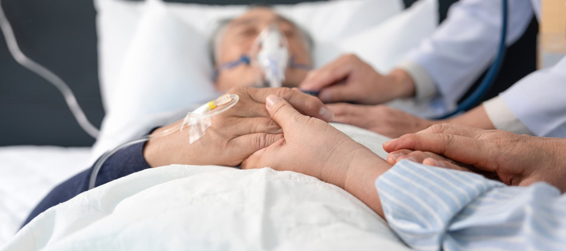 A photo of a man in a hospital bed holding loved ones' hands