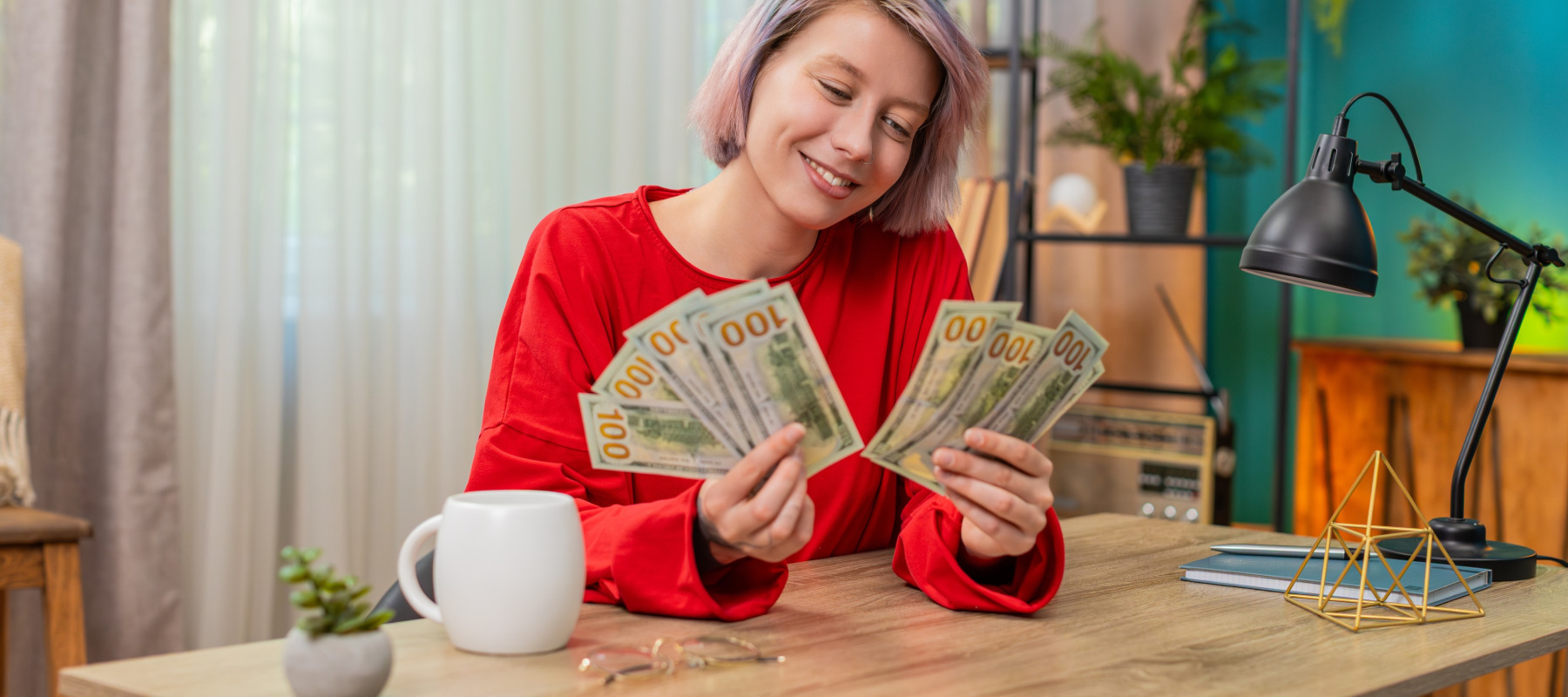Young white woman counts hundred dollar bills at her kitchen table.