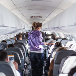 Interior of airplane with passengers in their seats and a female traveler walking the aisle.