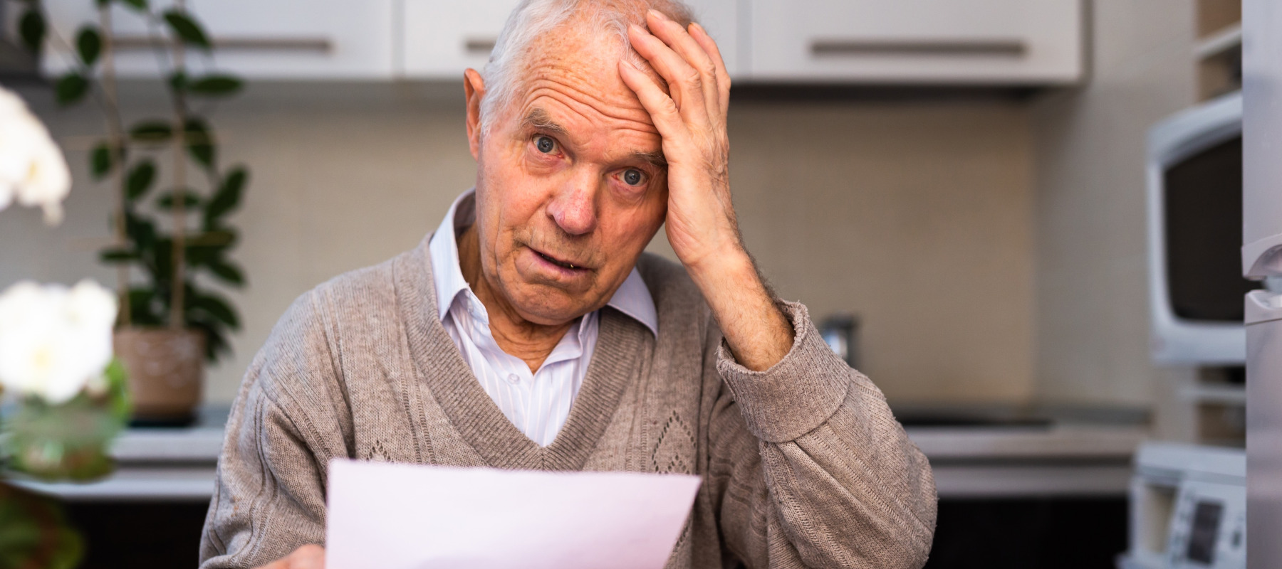 Old gray haired man sitting at table and stunned by paper notice.