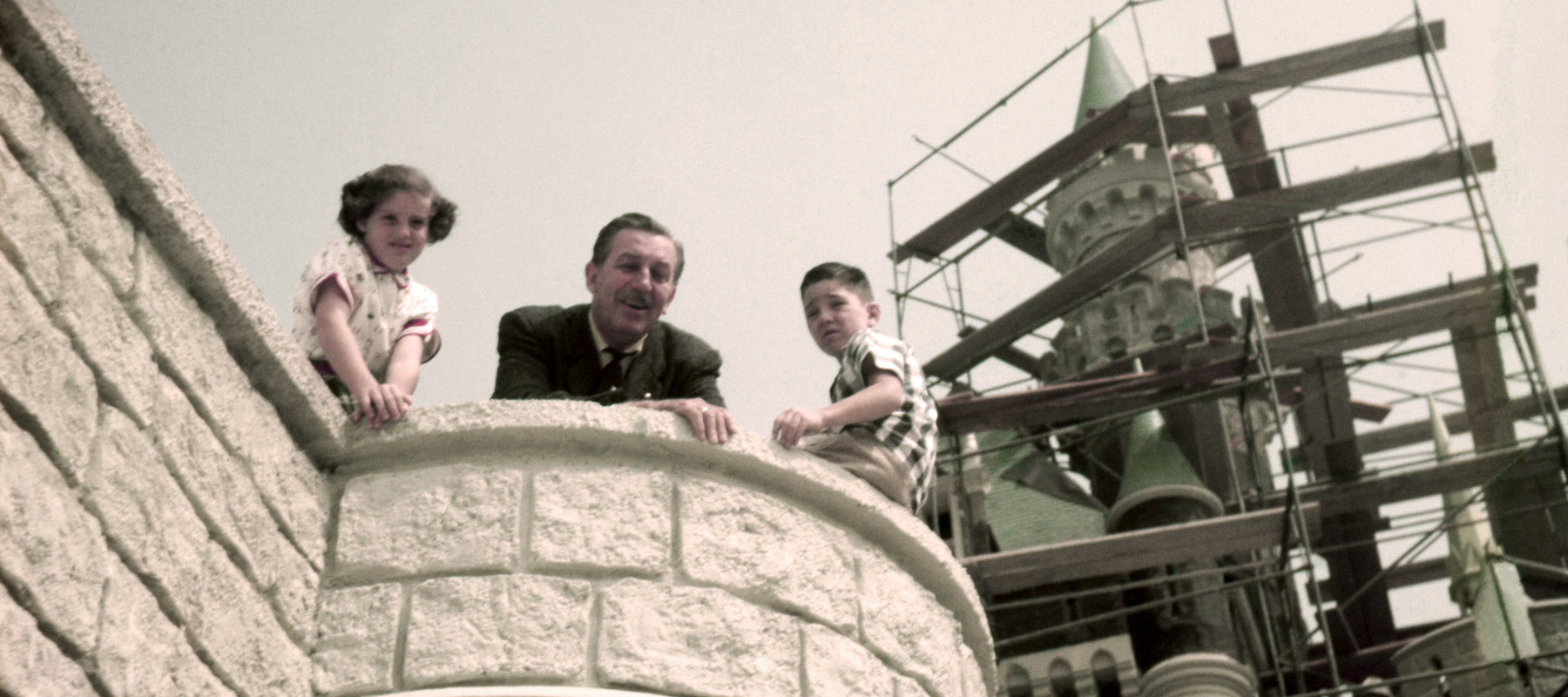 Walt Disney with two children as they look over a ledge during a tour of his Disneyland theme park, which officially opened several months later in March 1955.