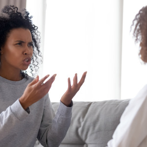 An upset woman holds her hands up in frustration while talking to another woman.