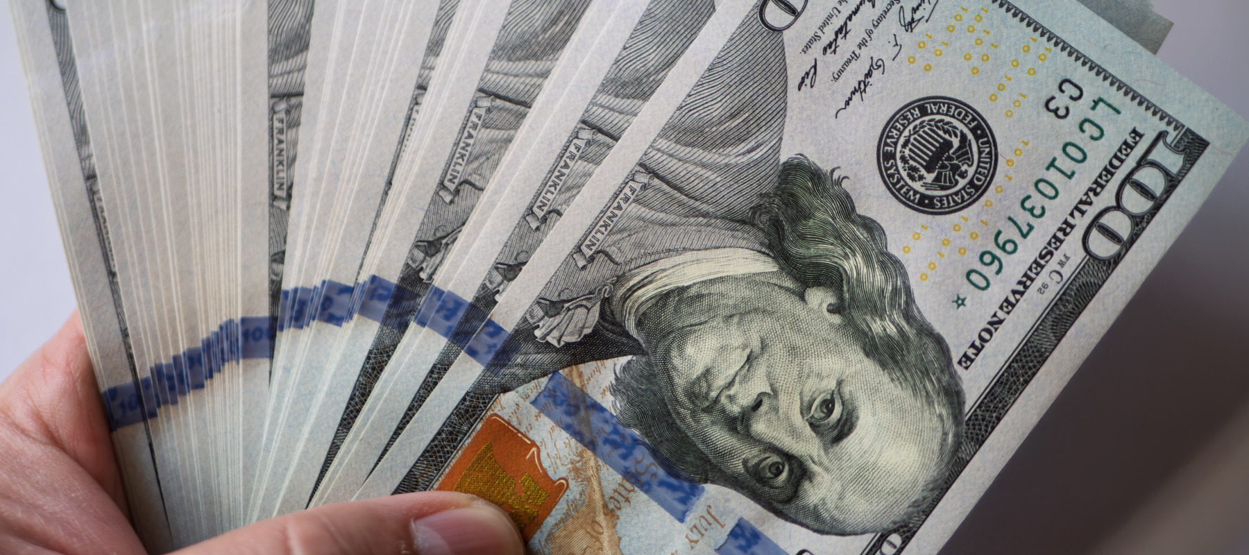 A large amount of U.S. $100 bills in a person's hand against a white background.
