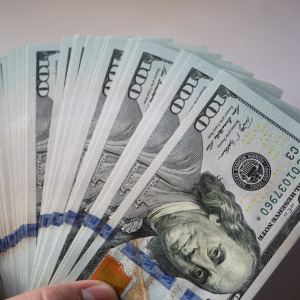 A large amount of U.S. $100 bills in a person's hand against a white background.