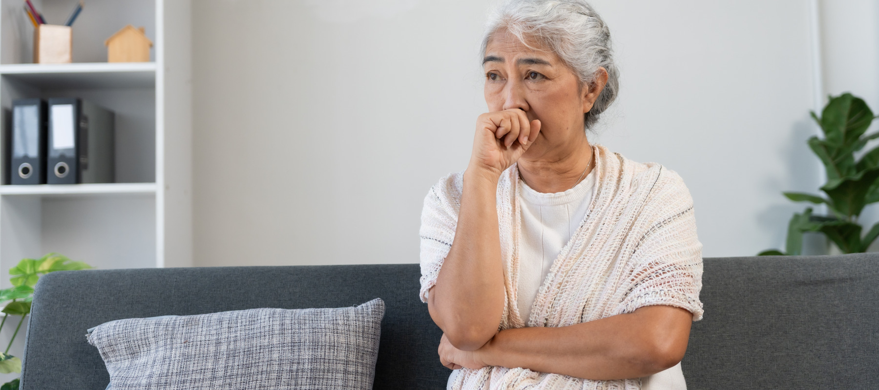 A concerned elderly woman sits on her couch.