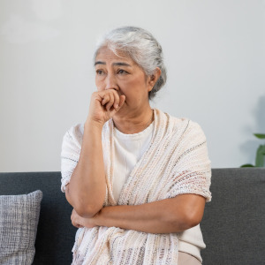 A concerned elderly woman sits on her couch.