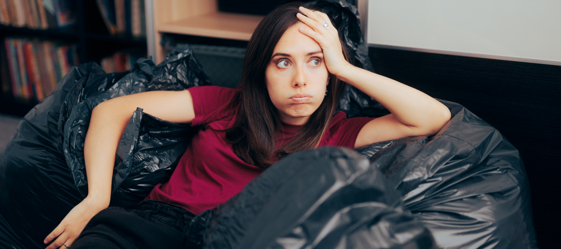 A woman sits on a pile of garbage bags with a frustrated expression.
