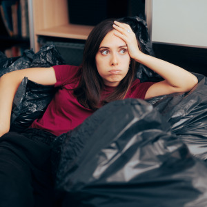 A woman sits on a pile of garbage bags with a frustrated expression.
