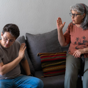An adult son and his mother raise their hands in frustration during a heated argument.