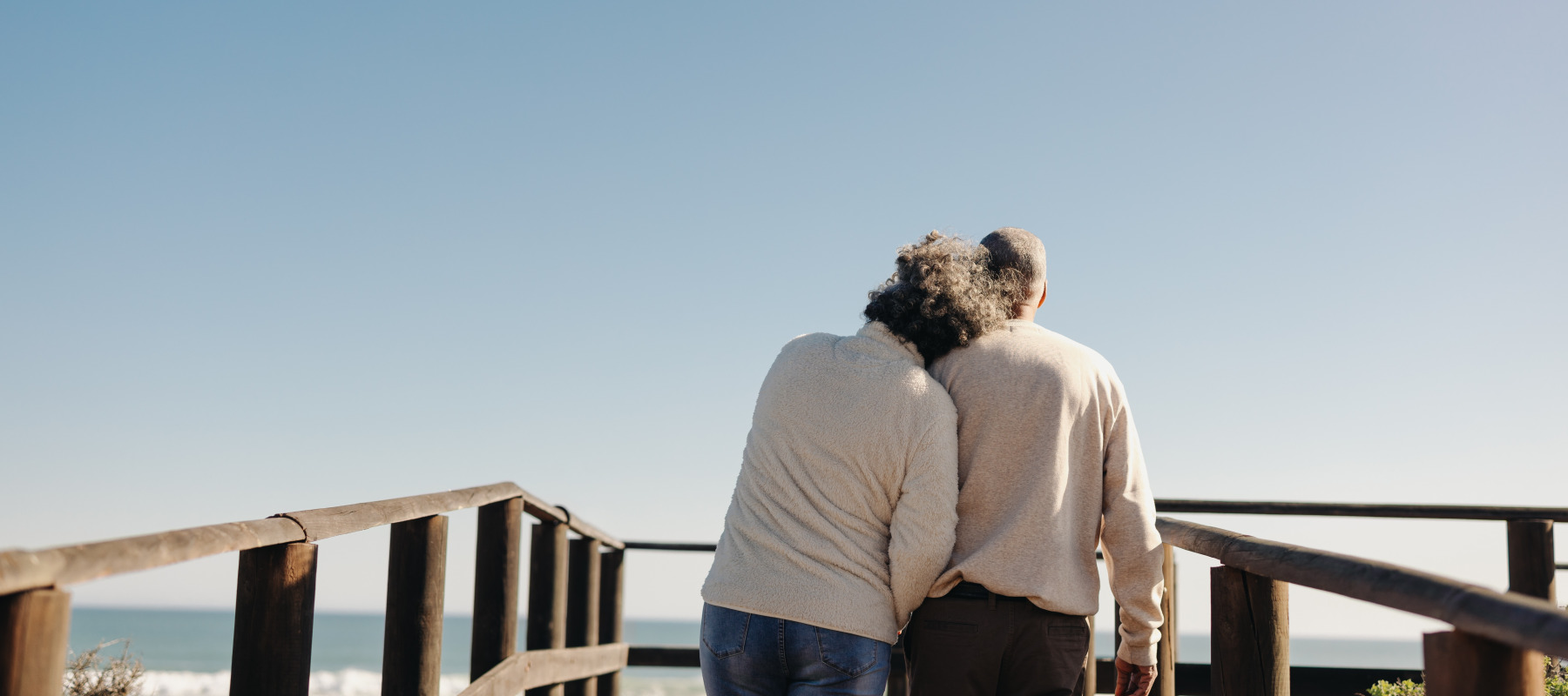 Rearview of a senior couple taking a walk along a wooden foot bridge at the beach.
