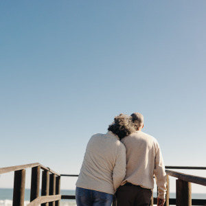 Rearview of a senior couple taking a walk along a wooden foot bridge at the beach.