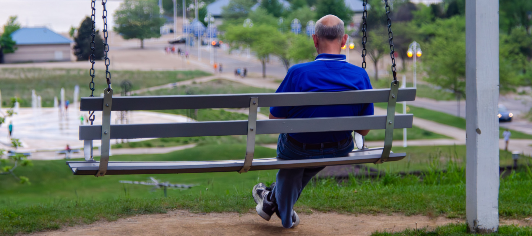Older man seen from behind, sitting on a porch swing.