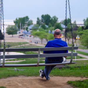 Older man seen from behind, sitting on a porch swing.