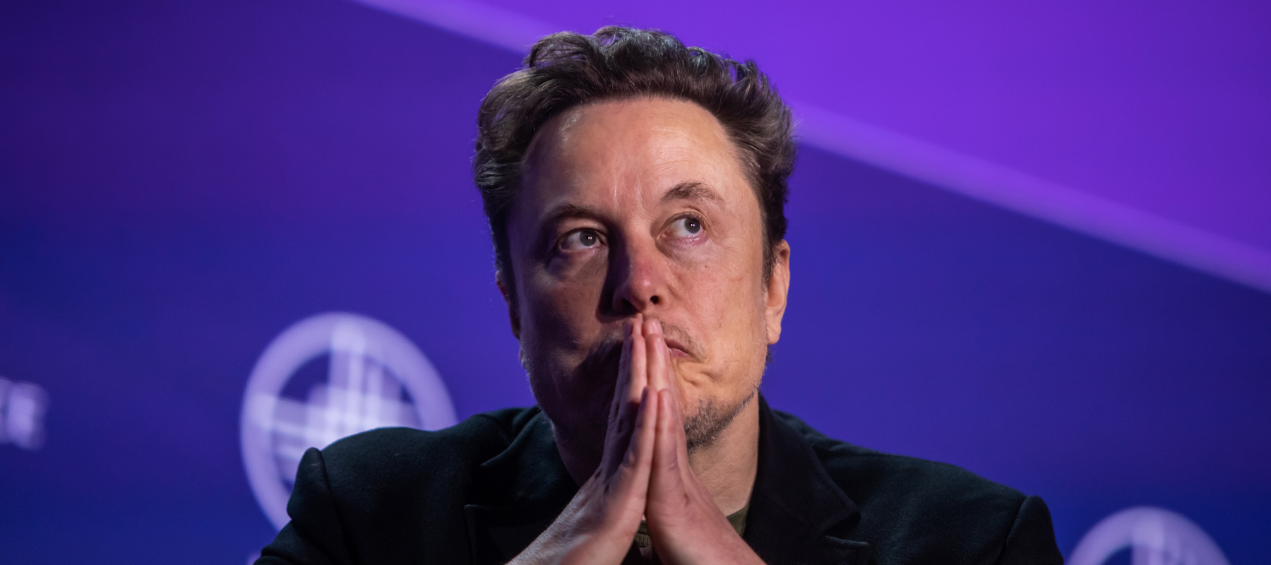 Elon Musk sits in a chair looking pensive.