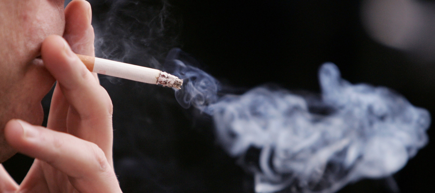 An unidentified man smokes a cigarette in the street outside his office.