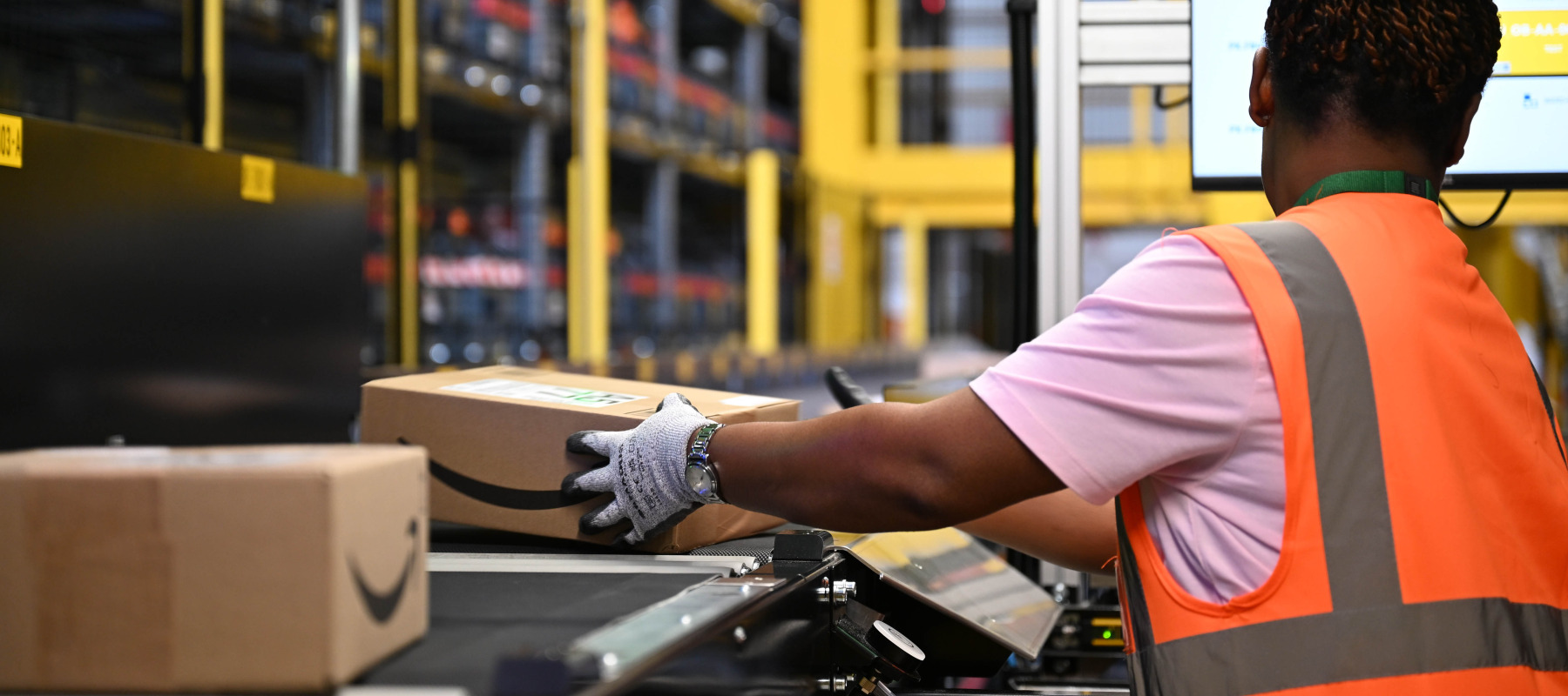 An Amazon employee places parcels from a conveyor belt into a box.