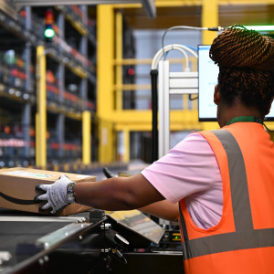 An Amazon employee places parcels from a conveyor belt into a box.