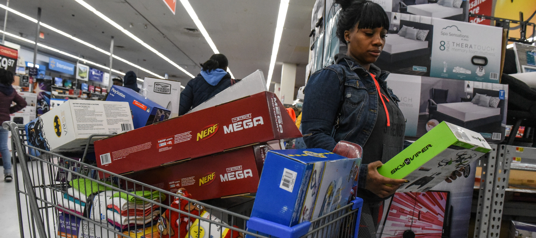 A woman shopping at Walmart with a loaded cart stops to look at an item.