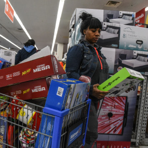 A woman shopping at Walmart with a loaded cart stops to look at an item.