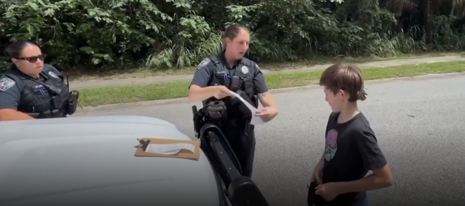 Police officers hold a citation and explain next steps to 11-year-old boy after stopping him on the road.