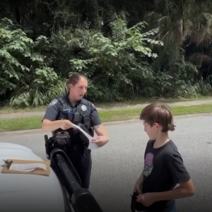 Police officers hold a citation and explain next steps to 11-year-old boy after stopping him on the road.