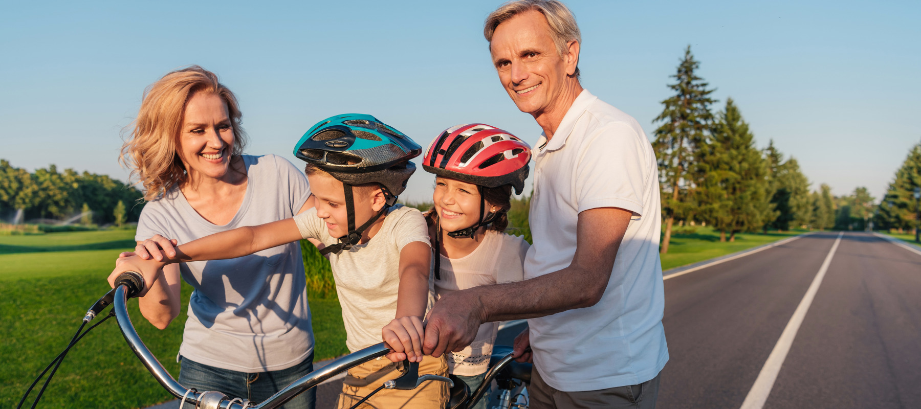 Two older parents or grandparents help their children or children ride their bikes.