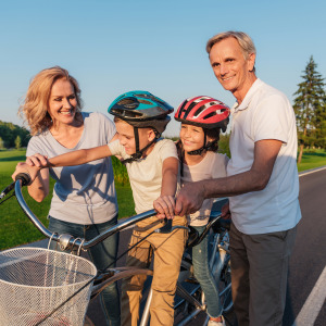 Two older parents or grandparents help their children or children ride their bikes.