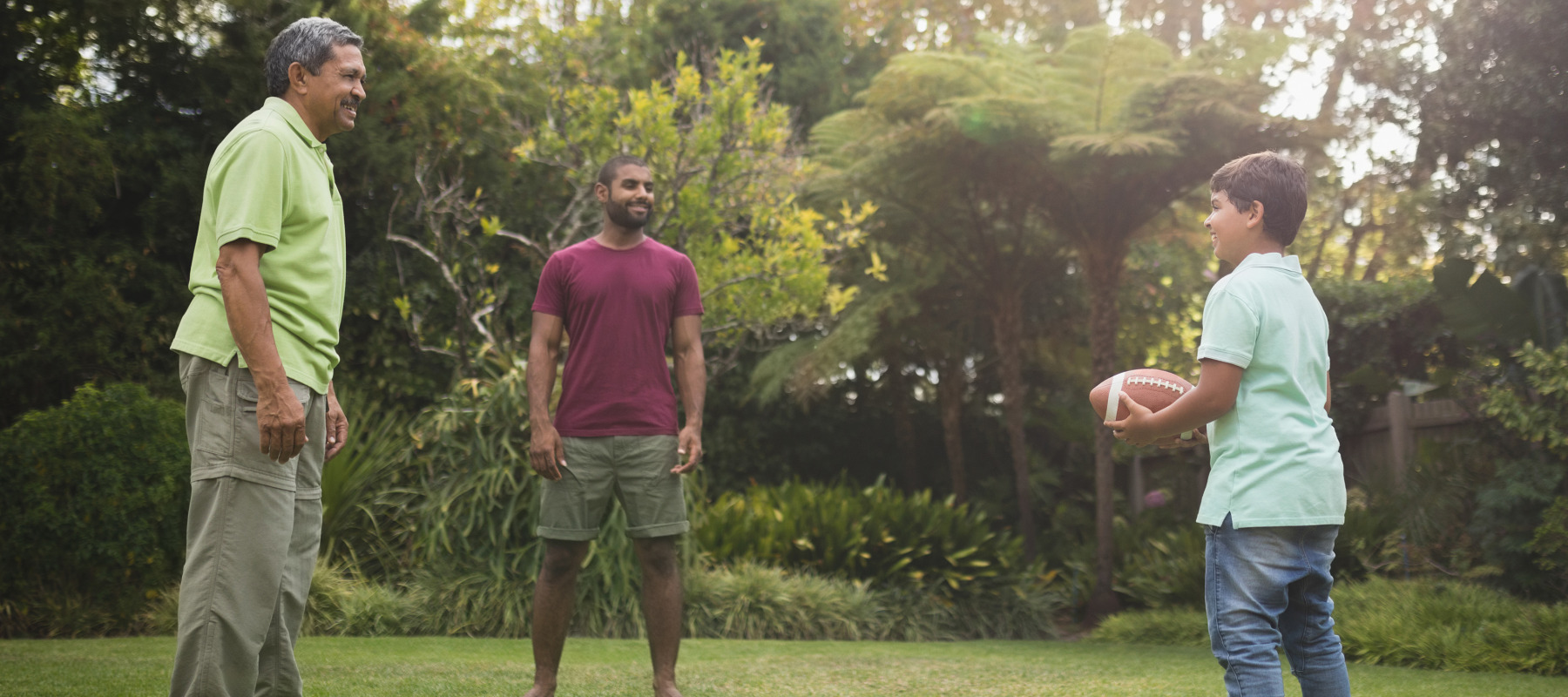 Three generations play football in a backyard.
