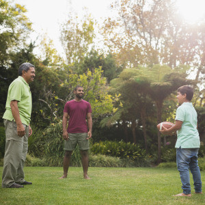 Three generations play football in a backyard.