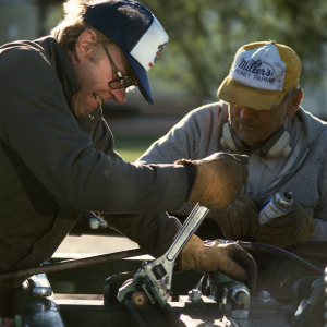 Two brothers, who are farmers, repair a plow on their property.