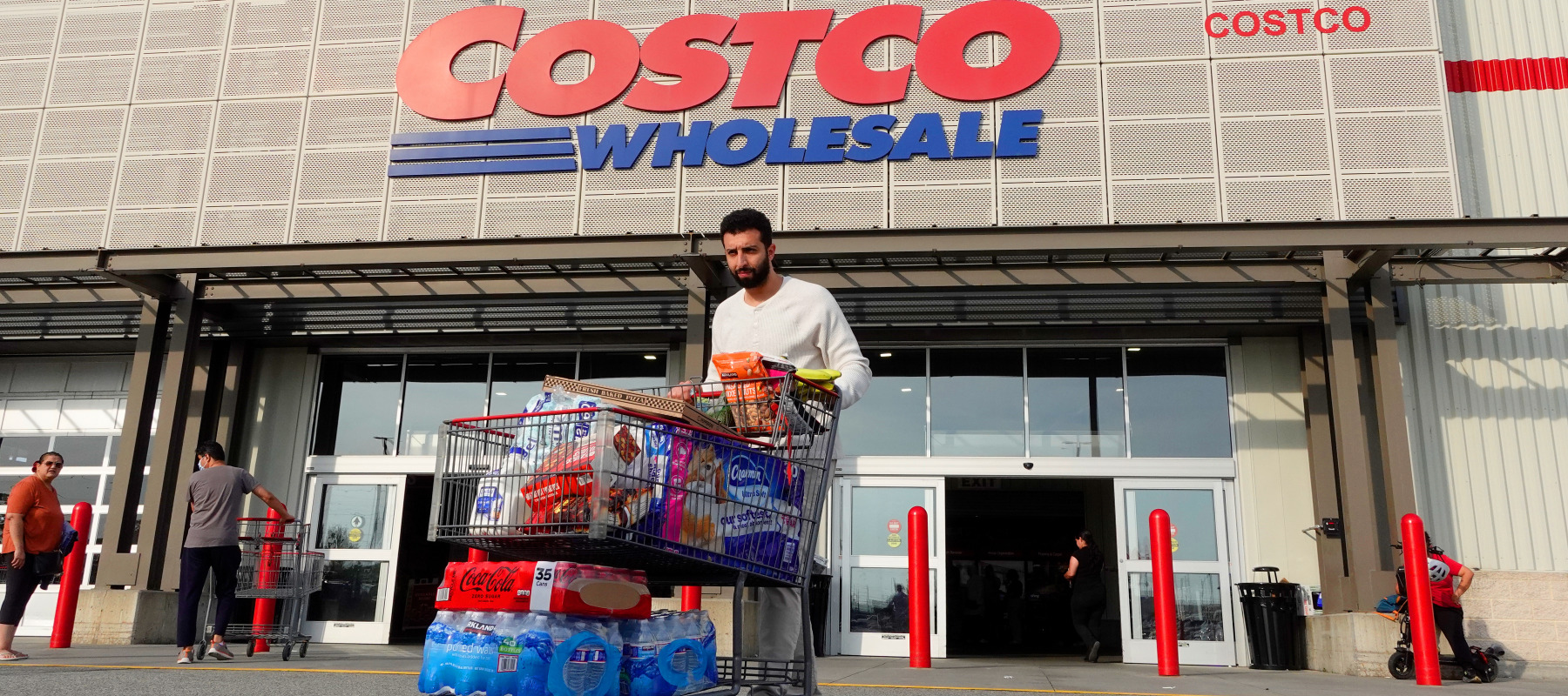 A person walks out of a Costco Wholesale store with a shopping cart of goods.