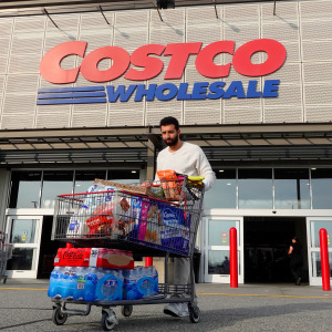 A person walks out of a Costco Wholesale store with a shopping cart of goods.