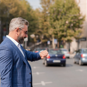 A businessman in a dapper suit looks at his watch while crossing the road.