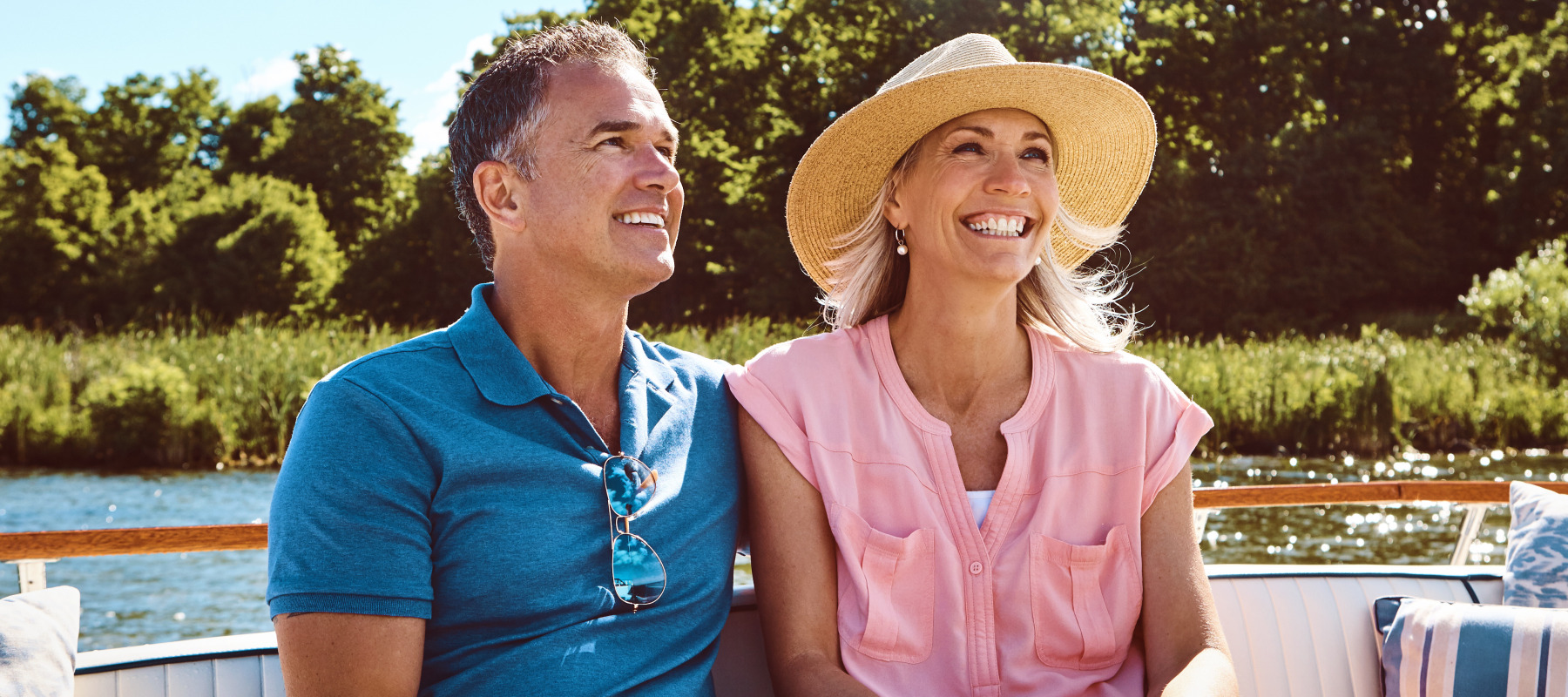 A wealthy middle-aged couple sit close together in a boat on a clear and bright summer's day.