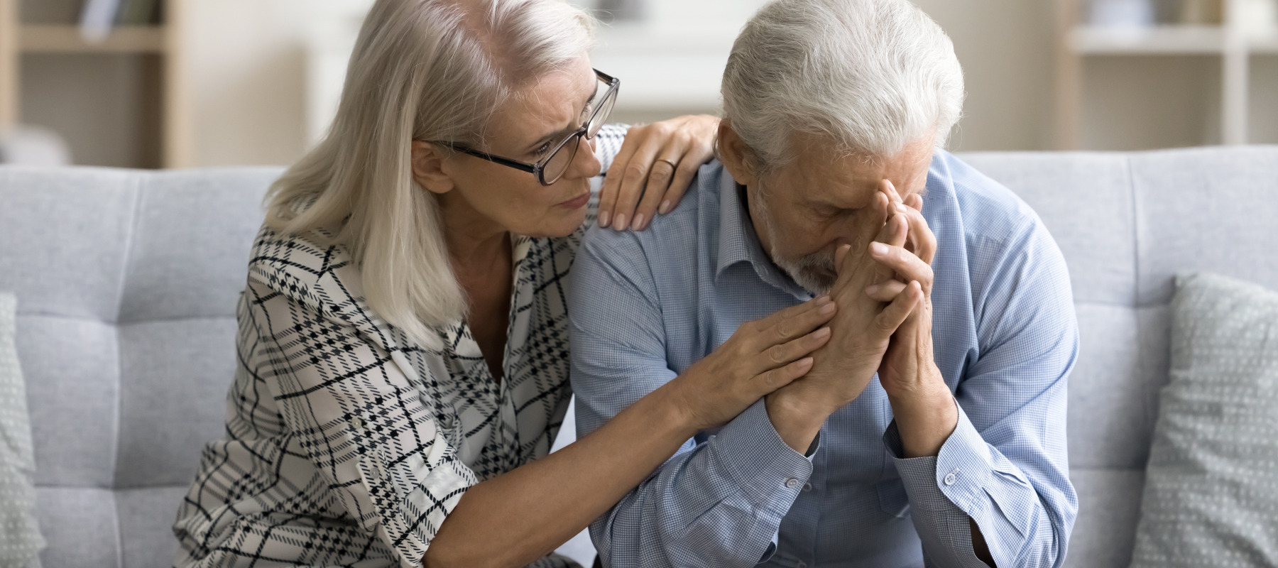 A woman comforts her distressed husband on the couch.