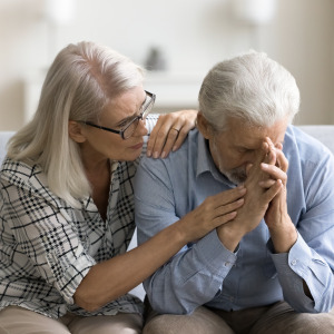 A woman comforts her distressed husband on the couch.