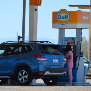 Woman in pink nurse scrubs pumps gas into her Subaru SUV.