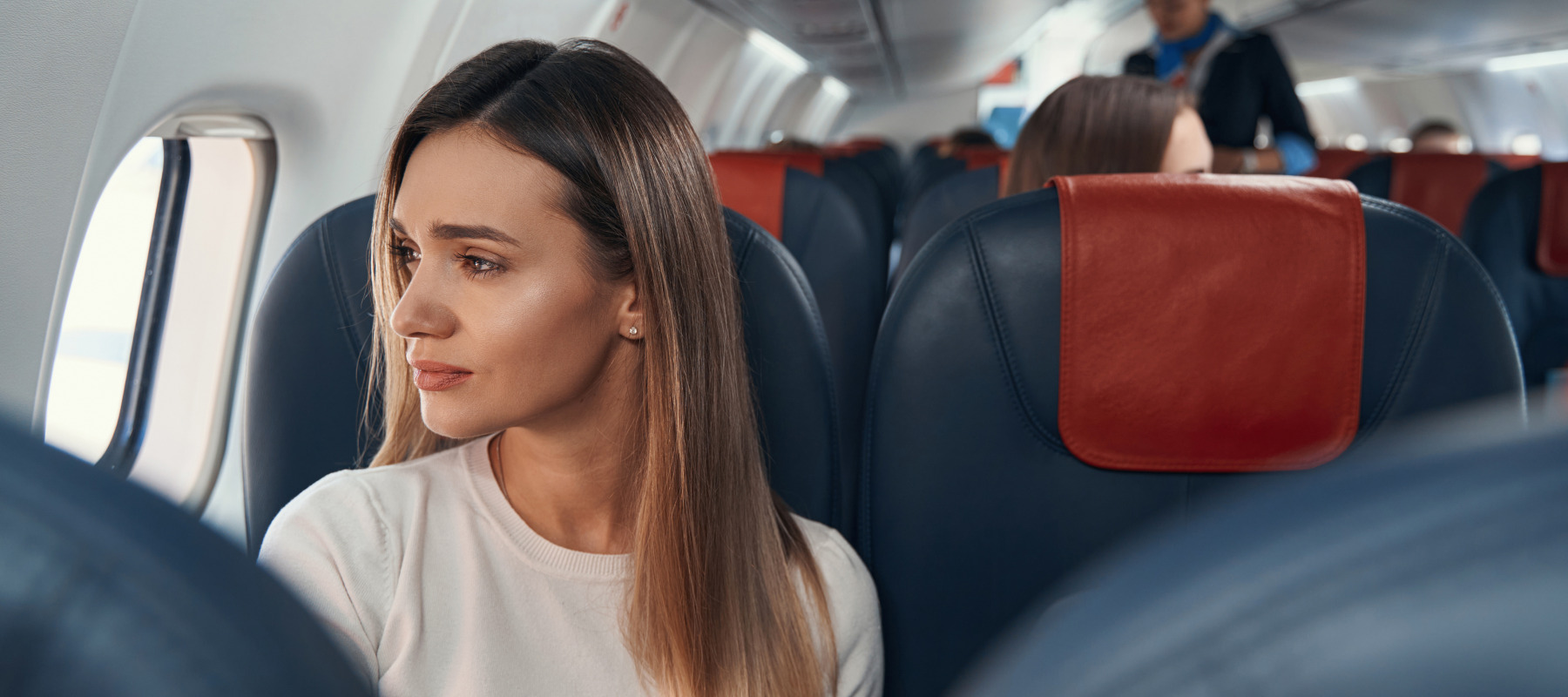 A young woman looks plaintively out the window of an airplane.