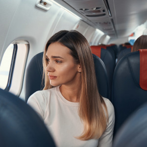 A young woman looks plaintively out the window of an airplane.